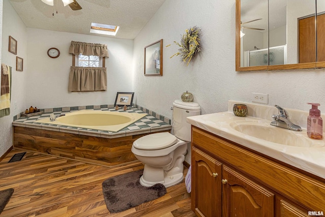 bathroom with wood finished floors, a skylight, a textured ceiling, a garden tub, and toilet