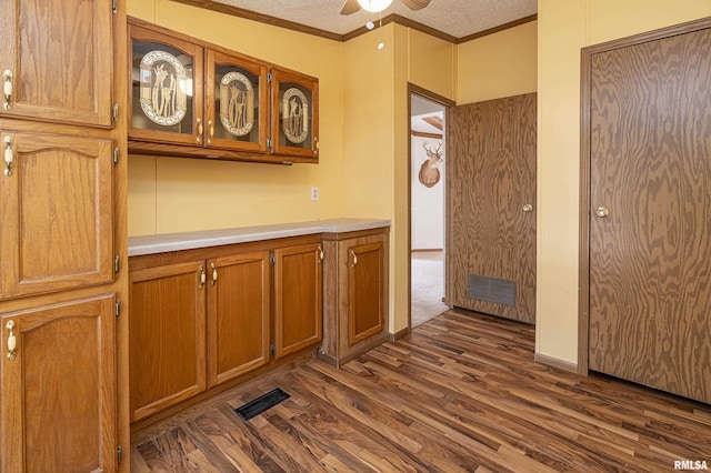 kitchen with visible vents, brown cabinets, ornamental molding, light countertops, and dark wood-style flooring