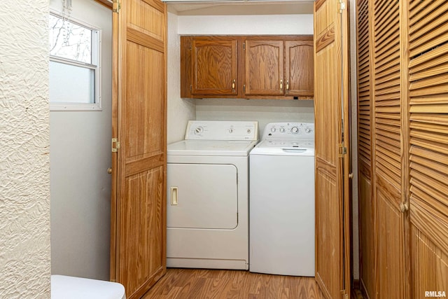 laundry area featuring a textured wall, cabinet space, independent washer and dryer, and light wood finished floors