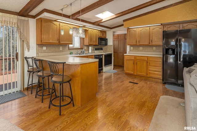 kitchen featuring lofted ceiling with beams, light countertops, light wood-style flooring, a peninsula, and black appliances