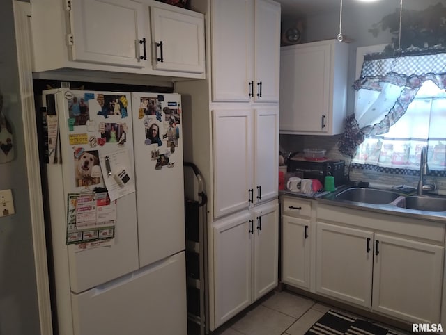 kitchen with light tile patterned flooring, white cabinetry, freestanding refrigerator, and a sink