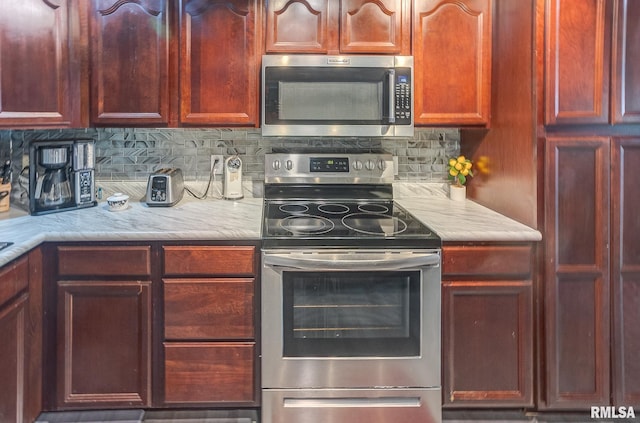 kitchen featuring decorative backsplash, stainless steel appliances, light countertops, and reddish brown cabinets