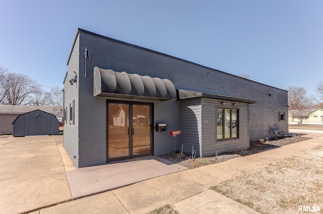 exterior space featuring an outbuilding, concrete driveway, concrete block siding, and a storage shed