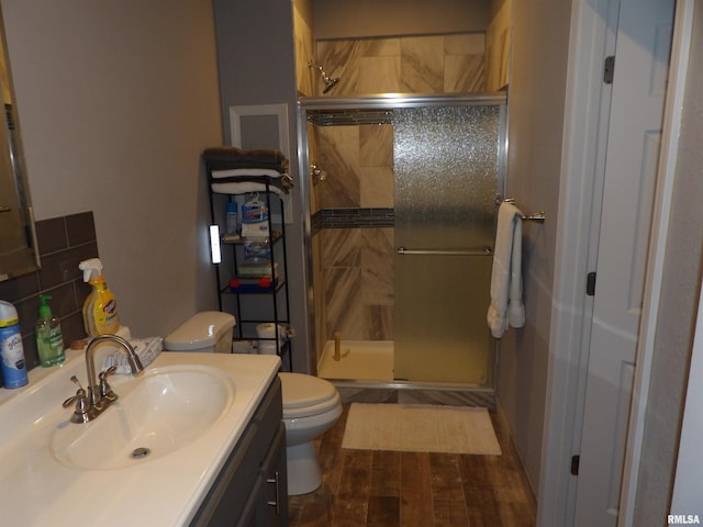 bathroom with toilet, decorative backsplash, a stall shower, wood finished floors, and vanity