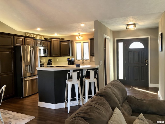 kitchen with dark wood finished floors, open floor plan, a breakfast bar area, light countertops, and stainless steel appliances