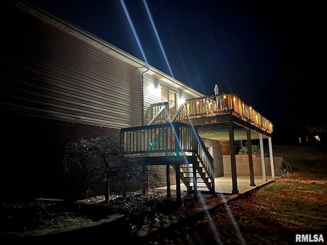 property exterior at twilight with a wooden deck, brick siding, stairs, and a patio area