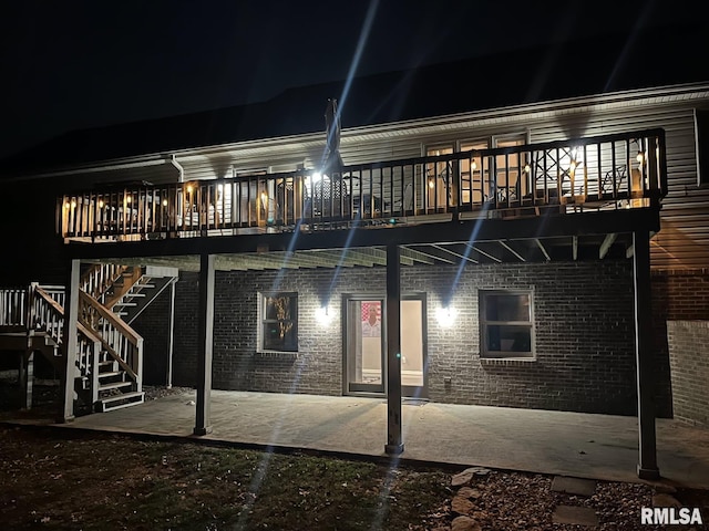 back of house at night with a patio area, stairway, and brick siding