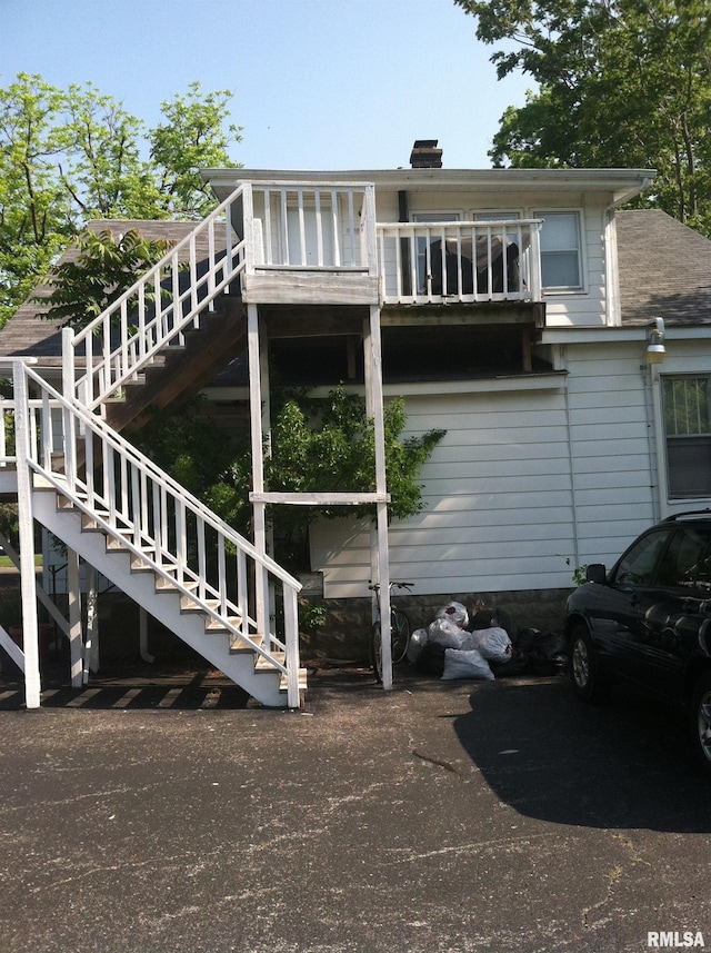 rear view of property featuring stairs, roof with shingles, and a chimney