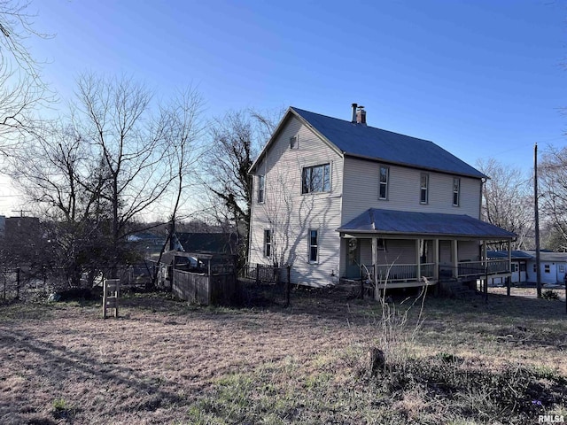 back of house with a porch, fence, and a chimney