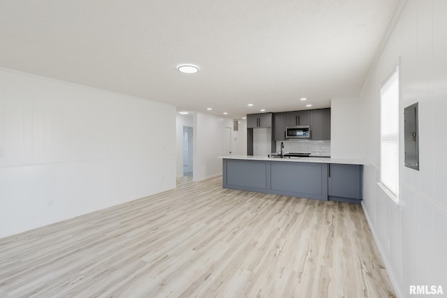kitchen with decorative backsplash, electric panel, light wood-type flooring, light countertops, and stainless steel microwave