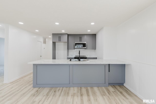 kitchen featuring gray cabinets, stainless steel microwave, a peninsula, and light stone countertops