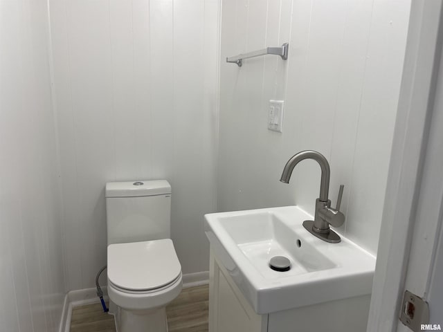 bathroom featuring baseboards, toilet, wood finished floors, and vanity