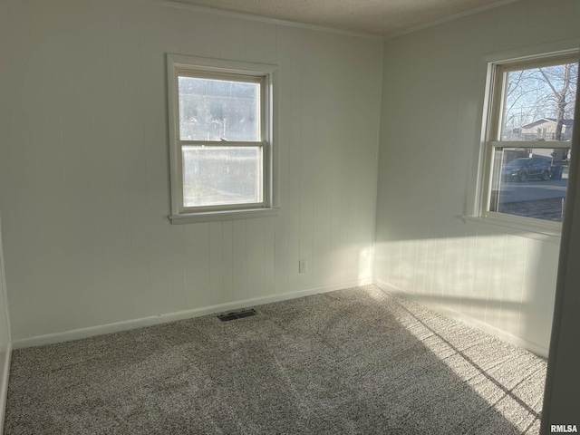 carpeted empty room with visible vents, crown molding, and baseboards