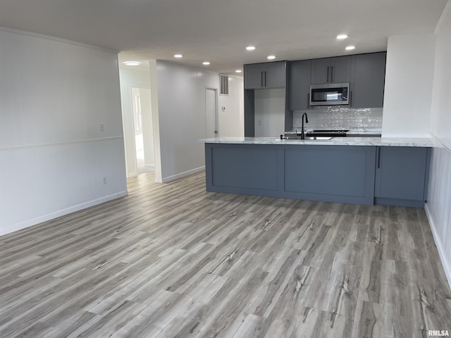 kitchen featuring stainless steel microwave, light wood-style floors, a peninsula, and decorative backsplash