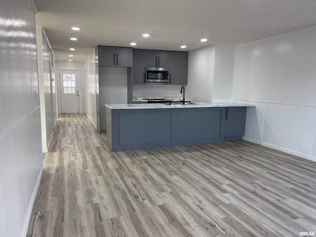 kitchen featuring stainless steel microwave, a peninsula, light wood-style floors, and a sink