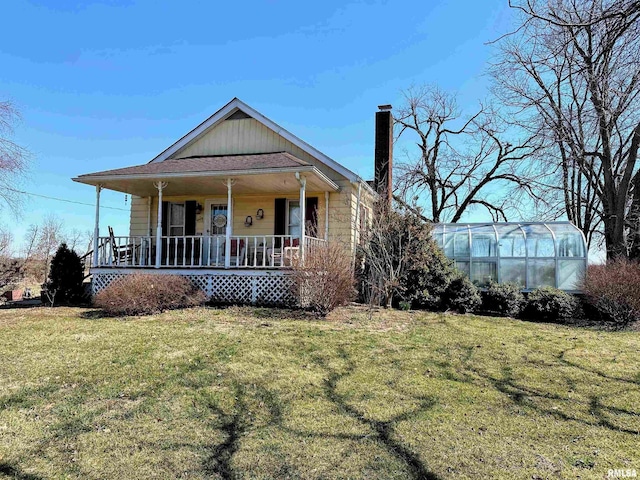 view of front of property with an outbuilding, a porch, a greenhouse, a front yard, and a chimney