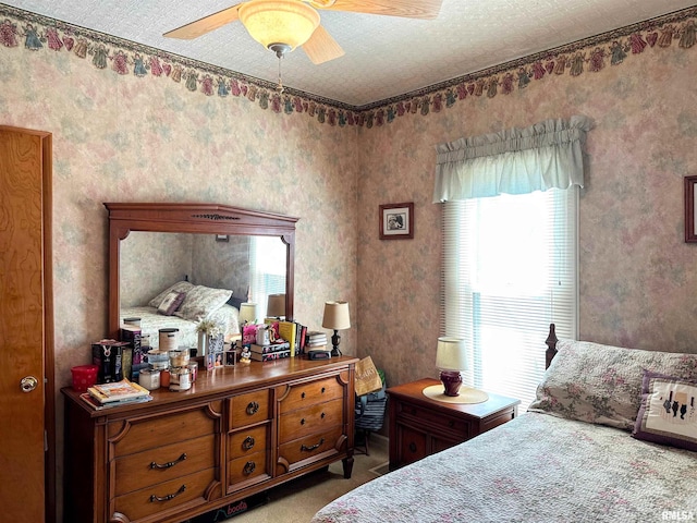 bedroom with a textured ceiling, wallpapered walls, a ceiling fan, and carpet floors