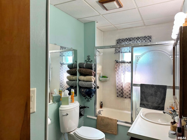 bathroom with vanity, visible vents, bath / shower combo with glass door, a drop ceiling, and toilet