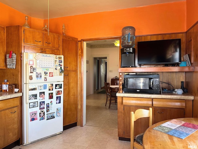 kitchen with brown cabinetry, light countertops, freestanding refrigerator, and black microwave