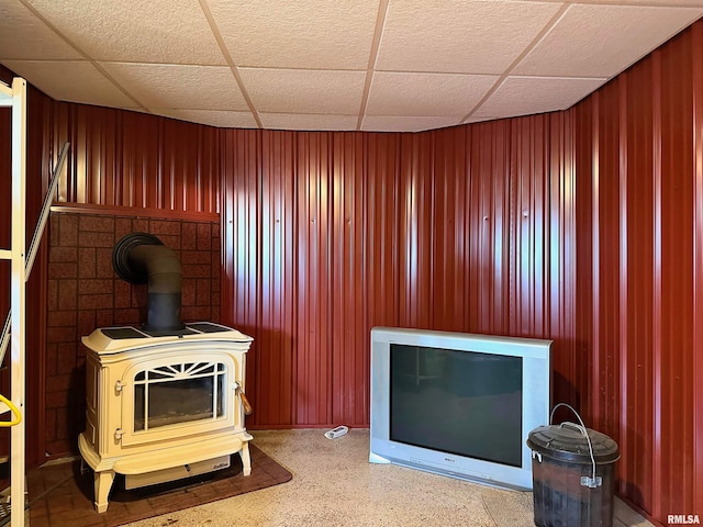 interior space with wooden walls, a wood stove, and a drop ceiling