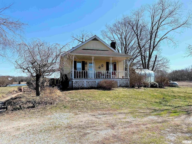 bungalow featuring a porch, a chimney, and a front lawn