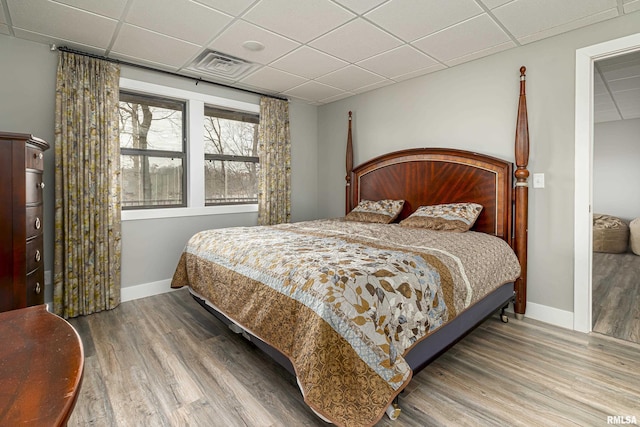 bedroom with a paneled ceiling, visible vents, baseboards, and wood finished floors