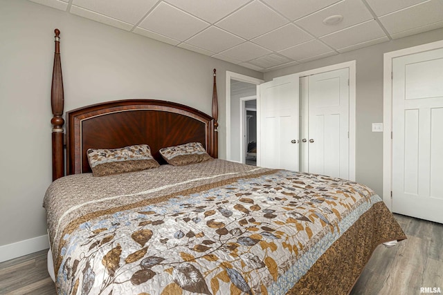 bedroom with a closet, a paneled ceiling, baseboards, and wood finished floors