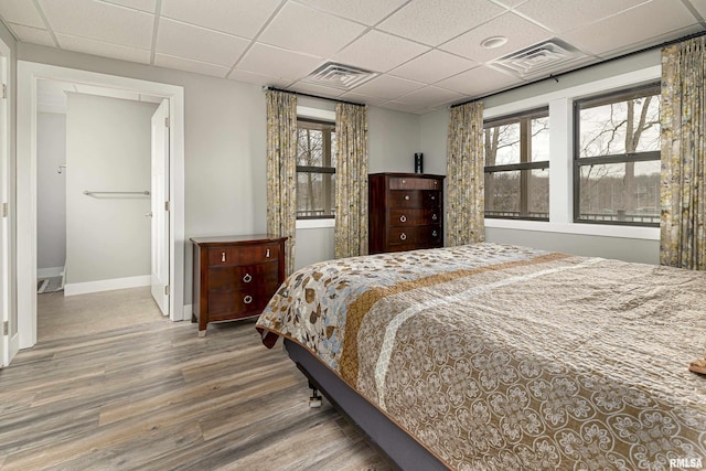 bedroom featuring baseboards, wood finished floors, visible vents, and a paneled ceiling