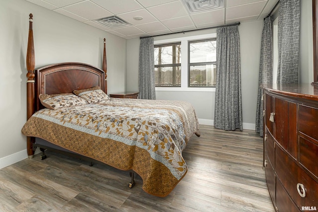 bedroom featuring a drop ceiling, visible vents, baseboards, and wood finished floors