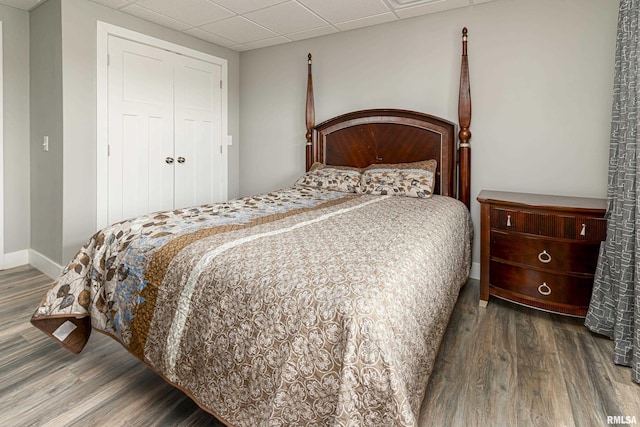 bedroom featuring a closet, a drop ceiling, baseboards, and wood finished floors