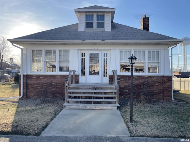 bungalow featuring brick siding, a chimney, and roof with shingles