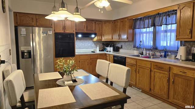 kitchen featuring black appliances, a sink, under cabinet range hood, brown cabinetry, and decorative backsplash