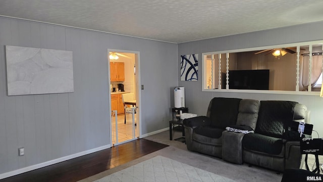 living area featuring baseboards, a textured ceiling, a ceiling fan, and wood finished floors