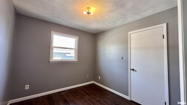 empty room featuring visible vents, dark wood-style floors, baseboards, and a textured ceiling