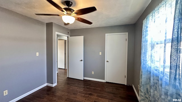 unfurnished bedroom featuring baseboards, a textured ceiling, dark wood-style floors, and a ceiling fan