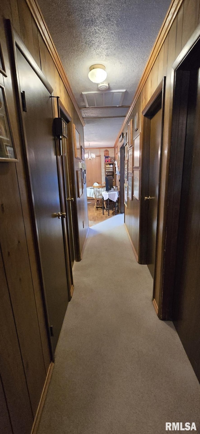 corridor with a textured ceiling, ornamental molding, carpet flooring, and wood walls