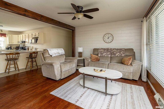 living area with visible vents, wooden walls, beamed ceiling, dark wood-style floors, and a ceiling fan