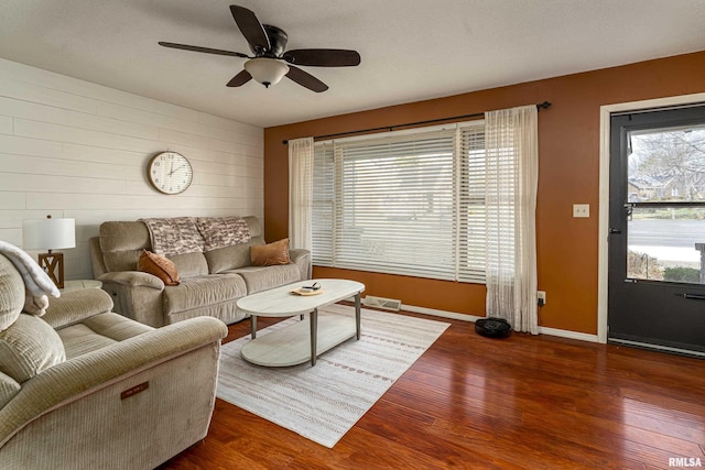 living room featuring ceiling fan, visible vents, baseboards, and wood finished floors