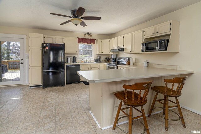 kitchen featuring black appliances, a ceiling fan, under cabinet range hood, a peninsula, and light countertops