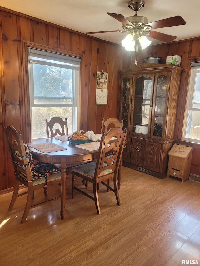 dining room with light wood-style flooring, wooden walls, and a ceiling fan