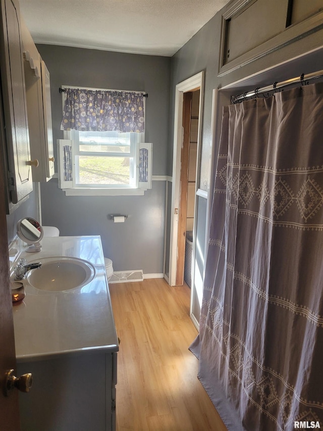 bathroom featuring baseboards, toilet, a shower with shower curtain, wood finished floors, and vanity