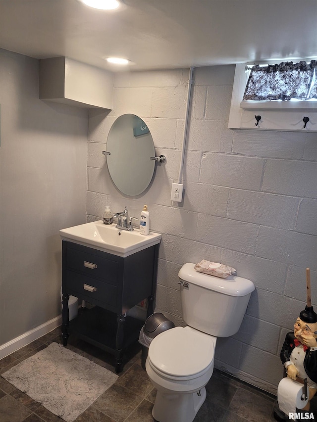 half bathroom with concrete block wall, toilet, and vanity