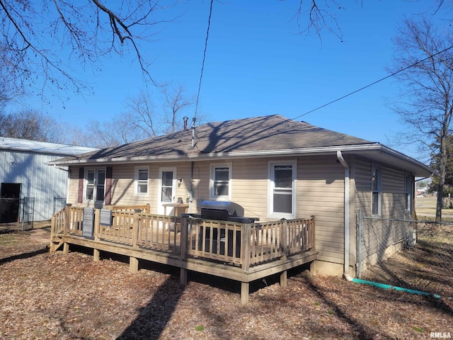 back of property with a wooden deck, a shingled roof, and fence