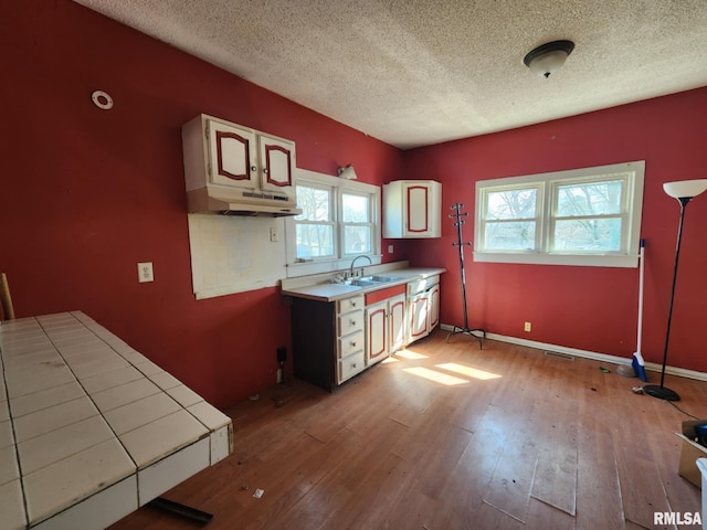 kitchen with baseboards, tile counters, wood finished floors, a textured ceiling, and a sink