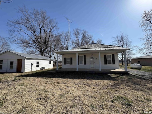 view of front facade featuring a front lawn, a standing seam roof, a porch, an outdoor structure, and metal roof