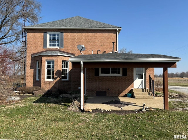 rear view of house with brick siding, entry steps, a yard, and roof with shingles