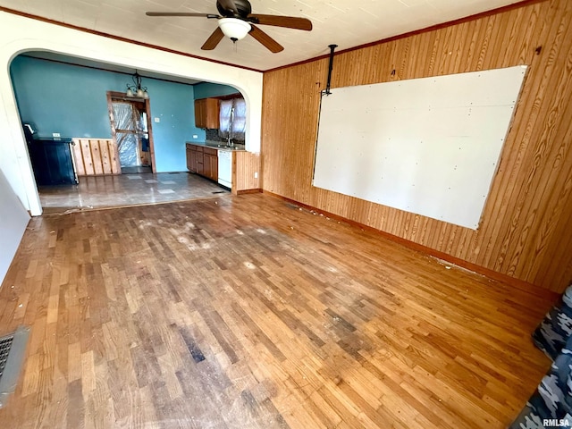 unfurnished living room with visible vents, wooden walls, ceiling fan, wood finished floors, and arched walkways