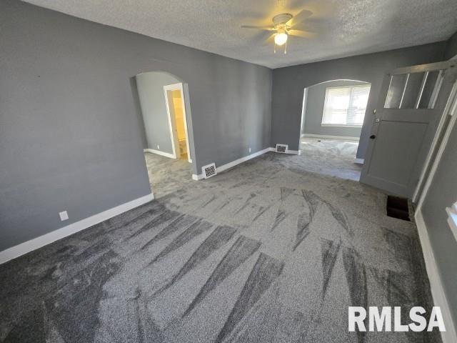 carpeted empty room featuring visible vents, a ceiling fan, arched walkways, and a textured ceiling