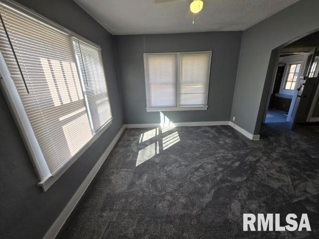 unfurnished room with arched walkways, dark carpet, a ceiling fan, and baseboards