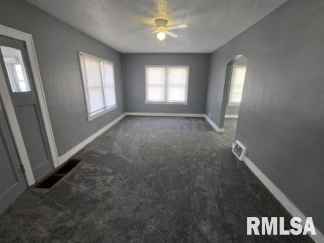 empty room featuring baseboards, arched walkways, ceiling fan, a textured ceiling, and dark carpet